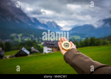 Women hand using a compass in the mountains, travel concept. Hand with compass at mountain road, background of mountains in summer, point of view. Stock Photo