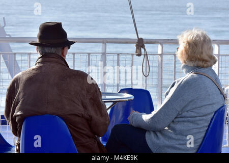 an old or elderly aging couple or man and woman husband and wife sitting at a table on an isle of wight ferry crossing next to the seaside and railing Stock Photo