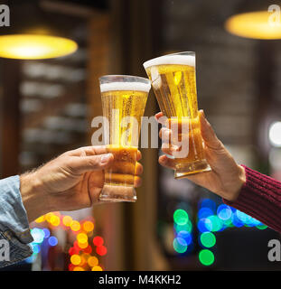 Beer glasses raised in a toast. Close-up hands with glasses. Blurred bar interior at the background. Stock Photo