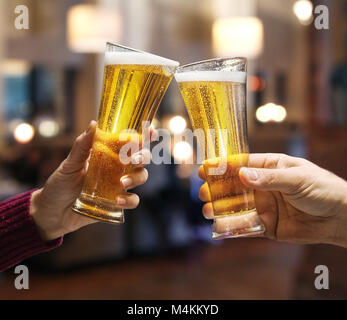 Beer glasses raised in a toast. Close-up hands with glasses. Blurred bar interior at the background. Stock Photo