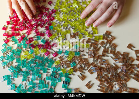 Woman hand sorting car electric parts colorful mini fuses on desk. Soft focus. Stock Photo
