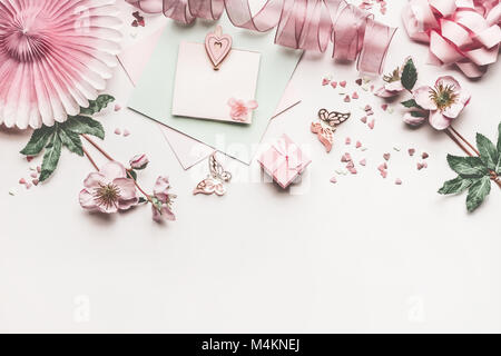 Beautiful pastel pink layout with flowers decoration, ribbon, hearts, bow and card mock up on white desk background, top view, flat lay, border. Weddi Stock Photo