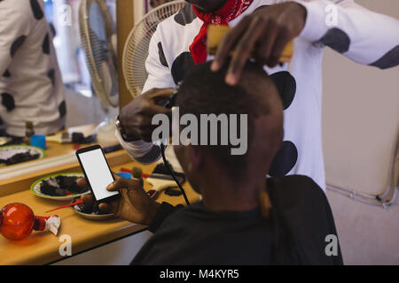 Customer using mobile phone while barber trimming his hair Stock Photo