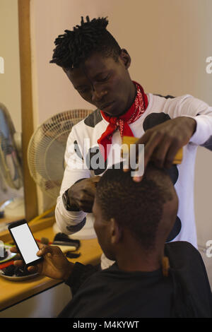 Customer using mobile phone while barber trimming his hair Stock Photo