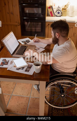 Disabled man noting while using laptop Stock Photo