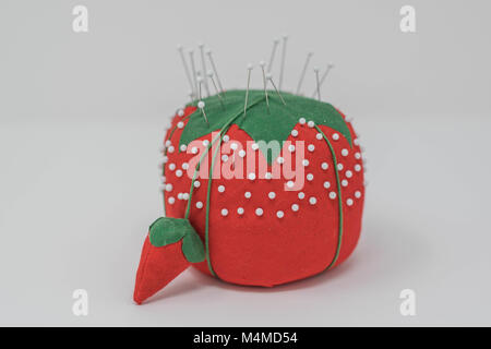 Isolated, close-up shot of a pin cushion that resembles a strawberry, with white glass pins stuck in it Stock Photo