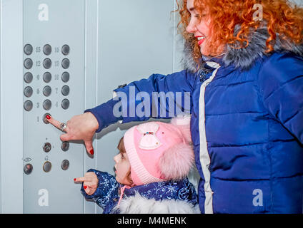 Mom and daughter went to the Elevator and press the button to go down. Stock Photo
