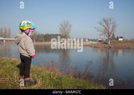 Baby girl standing on the bank of the river Elbe in a sunny day with blue sky. Stock Photo