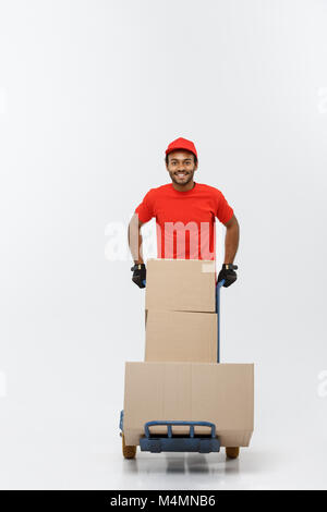 Delivery Concept - Portrait of Handsome African American delivery man or courier pushing hand truck with stack of boxes. Isolated on Grey studio Background. Copy Space. Stock Photo