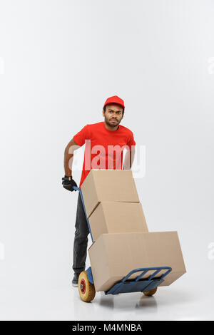 Delivery Concept - Portrait of Handsome African American delivery man or courier pushing hand truck with stack of boxes. Isolated on Grey studio Background. Copy Space. Stock Photo