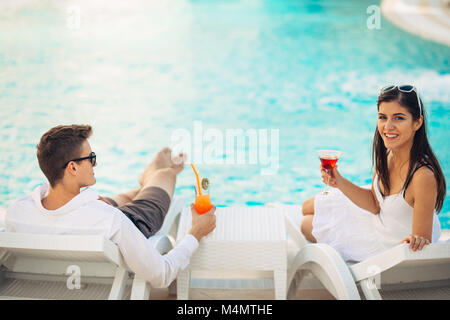 Positive happy couple relaxing by the pool in luxury summer vacation resort.Drinking cocktails.Enjoying time together in spa wellness center.Summertim Stock Photo