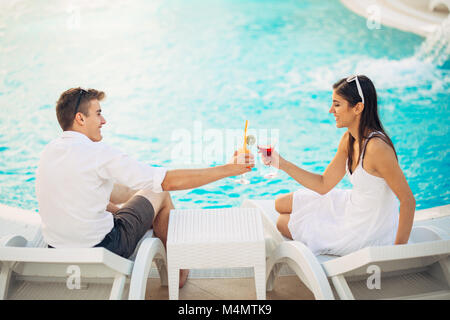 Positive happy couple having a romantic afternoon by the pool in luxury summer vacation resort.Drinking cocktails.Relaxing and enjoying spa wellness Stock Photo