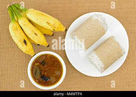 Plate of Puttu (popular south Indian breakfast dish) with chickpeas curry and bananas on a jute mat. Stock Photo