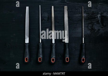 Series of many sharp steel blades on black wooden background. Set of chisels. Top view. Copy space. Still life. Flat lay Stock Photo