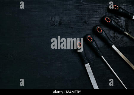 Series of many sharp steel blades on black wooden background. Set of chisels. Top view. Copy space. Still life. Flat lay Stock Photo