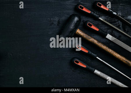 Series of many sharp steel blades and hammer on black wooden background. Set of chisels. Top view. Copy space. Still life. Flat lay Stock Photo