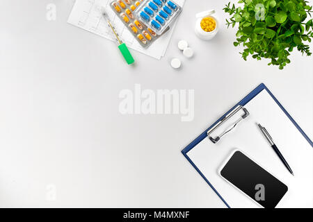 Top view of doctor's desk table, blank paper on clipboard with pen, electronic thermometer and tablets in capsules. Copy space. Designer's blank. Stil Stock Photo