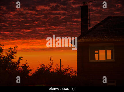 Fiery red sunset sky with clouds and a single house Stock Photo