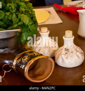 Horn for wine, salt and pepper shakers in a form of khinkali and spinach in a bowl on the table Stock Photo