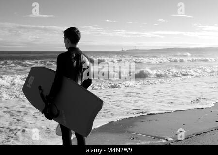 Male Bodyboarder Contemplating the Water before Surfing the Cold North Sea Waves at Aberdeen Beach, Scotland, UK. Winter 2018. Stock Photo