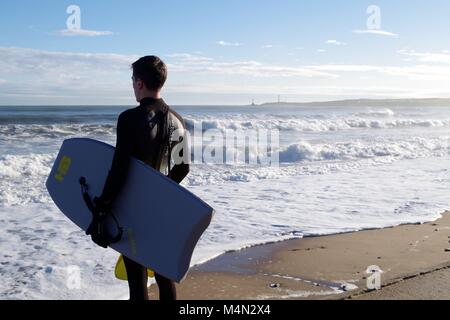 Male Bodyboarder Contemplating the Water before Surfing the Cold North Sea Waves at Aberdeen Beach, Scotland, UK. Winter 2018. Stock Photo