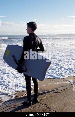 Male Bodyboarder Contemplating the Water before Surfing the Cold North Sea Waves at Aberdeen Beach, Scotland, UK. Winter 2018. Stock Photo