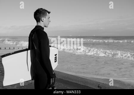 Male Bodyboarder Contemplating the Water before Surfing the Cold North Sea Waves at Aberdeen Beach, Scotland, UK. Winter 2018. Stock Photo