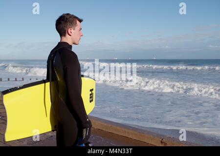 Male Bodyboarder Contemplating the Water before Surfing the Cold North Sea Waves at Aberdeen Beach, Scotland, UK. Winter 2018. Stock Photo