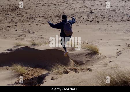 Young Man Leaping from a Sand Dune at Cruden Bay. Aberdeenshire, Scotland, UK. Winter, 2018. Stock Photo