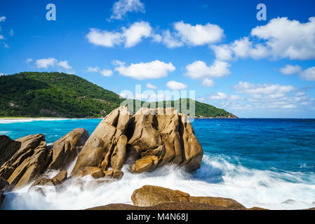 Splashing water withe big water fountains on a wild tropical beach with granite rocks, palm trees, turquoise water, white sand and blue sky. Police ba Stock Photo