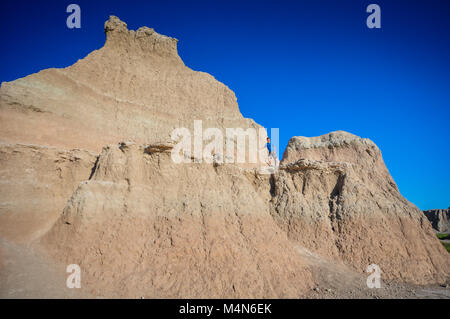 Young boy, wearing a turquoise shirt and shorts, climbs chalk ridge in the Badlands National Park in South Dakota on a vibrant blue sky sunny day. Stock Photo