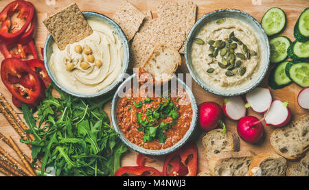 Vegan snack board. Flat-lay of various Vegetarian dips hummus, babaganush and muhammara with crackers, bread and fresh vegetables, wooden background, Stock Photo