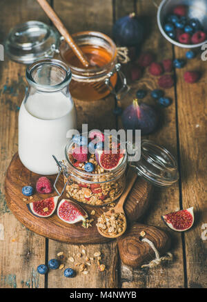 Healthy vegan breakfast. Oatmeal granola with bottled almond milk, honey, fresh fruit and berries on hoard over rustic wooden table background. Clean Stock Photo