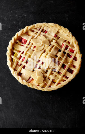 Pie crust design ideas - various ways of pie decoration with lattice and leaves. Apple, strawberry and raspberry pie uncooked on black table. Stock Photo
