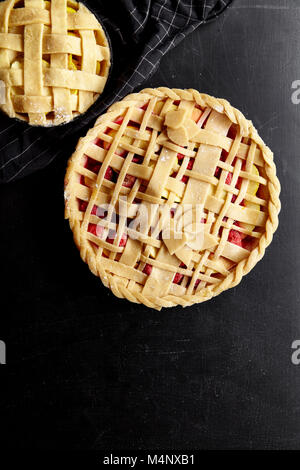 Pie crust design ideas - various ways of pie decoration with lattice and leaves. Apple, strawberry and raspberry pies uncooked on black table. Stock Photo
