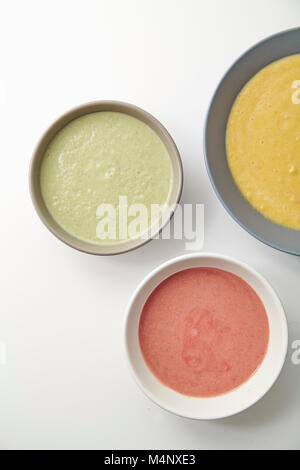 Flatlay with three bowls with colorful vegetarian creamy soups with broccoli, pumpkin and beetroot on white background Stock Photo