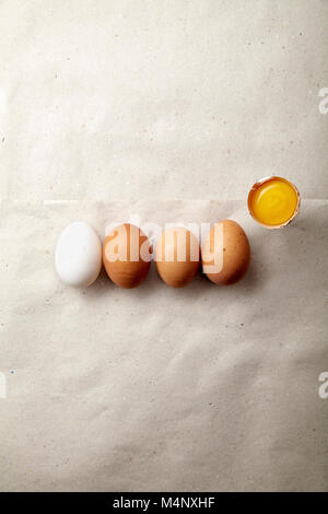 Four chicken eggs of different natural tint with one egg yolk on paper sheet Stock Photo