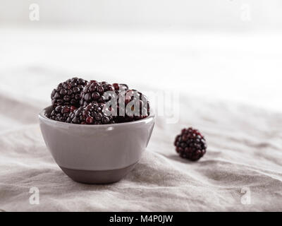 Small, gray bowl filled with fresh blackberries on a gray linen with a bright, airy background. Stock Photo