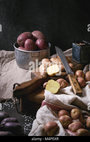Variety of raw uncooked organic potatoes different kind and colors red, yellow, purple on wooden cutting board with kitchen towels over black table. D Stock Photo