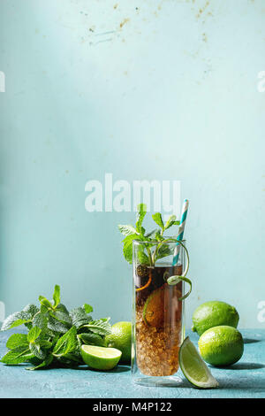 Glass of classic Cuba libre cocktail with lime, mint, crushed ice and cola, served with ingredients above and retro cocktail tubes over turquoise gree Stock Photo