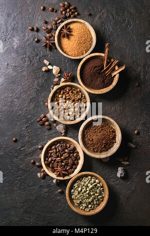 Variety of grounded, instant coffee, different coffee beans, brown sugar, spices in wooden bowls over dark texture background. Top view, space Stock Photo