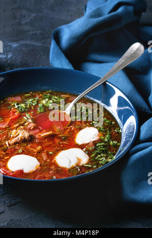 Plate of traditional beetroot borscht soup with sour cream and fresh coriander served with garlic bread buns pampushka with blue textile over dark blu Stock Photo