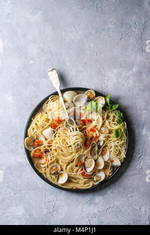 Pasta spaghetti Vongole in tomato cream sauce in black plate with fork over gray texture background. Top view, copy space Stock Photo