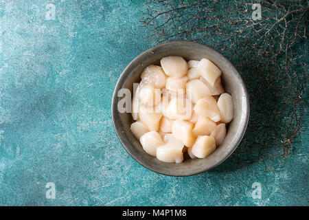 Raw uncooked scallops in vintage metal bowl over turquoise texture background. Top view, copy space Stock Photo