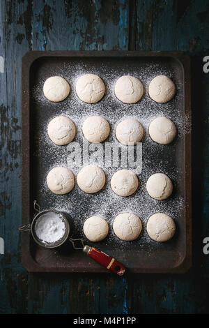 Homemade almond cookies with sugar powder, with vintage sieve, on old oven tray over dark blue wooden table. Dark rustic style. Top view, space Stock Photo