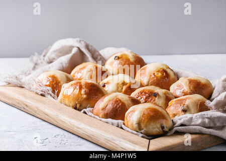 Homemade Easter traditional hot cross buns on wooden tray with textile over white texture background. Copy space Stock Photo