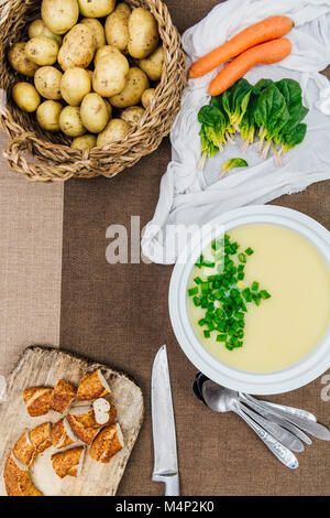 Cream of potato soup topped with chopped green onions in a white soup pot photographed from top view. Sliced Turkish simit on a wooden board, baby pot Stock Photo