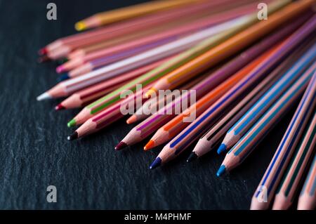 An array of coloring pencils spread out on a black slate Stock Photo
