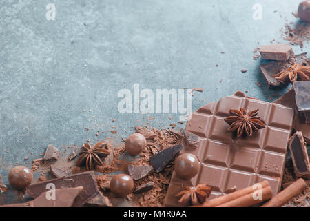 Broken chocolate bar with chunks of milk and bitter chocolate, spices and scattered cocoa on a stone background. Confectionery food photography. Desse Stock Photo
