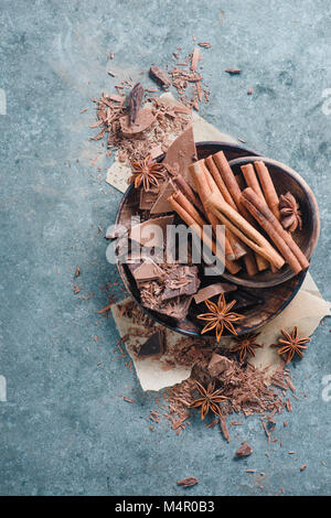 Frame with a wooden bowl filled with chocolate pieces, spices, anise stars, cinnamon and cocoa on a stone background. Ingredients for a dessert. Stock Photo